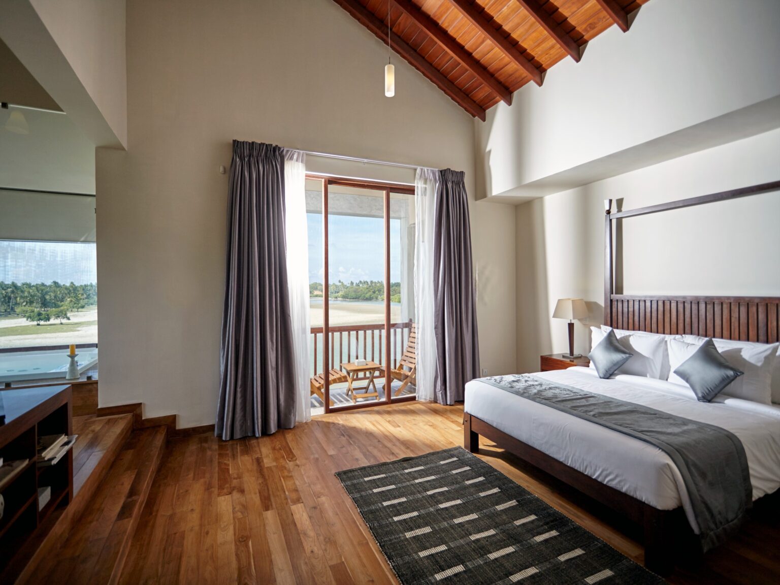 A suite bedroom with timber floors and a glass door to a balcony over the water