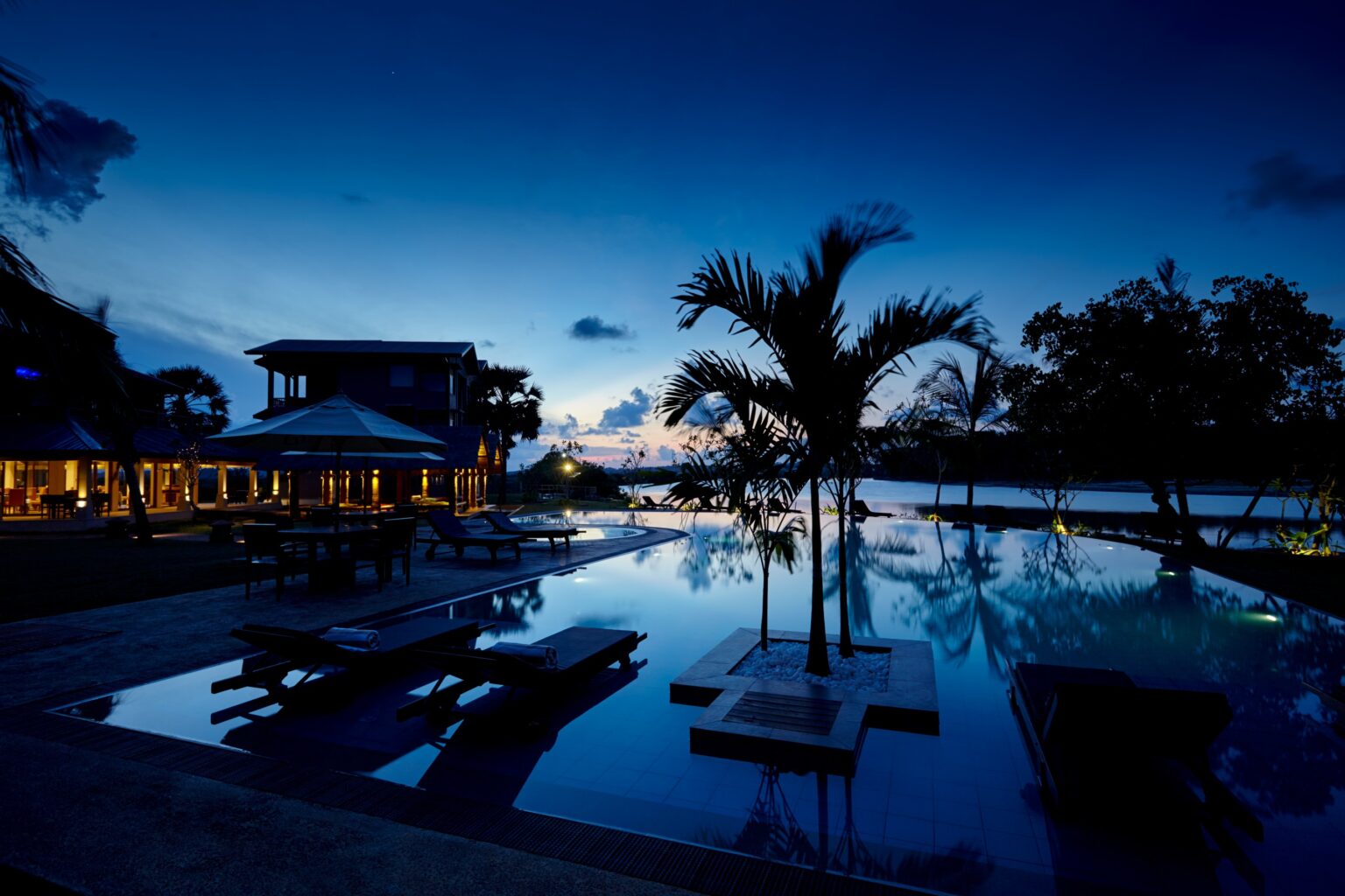 The pool and palms at dusk, with lights reflected in the still water